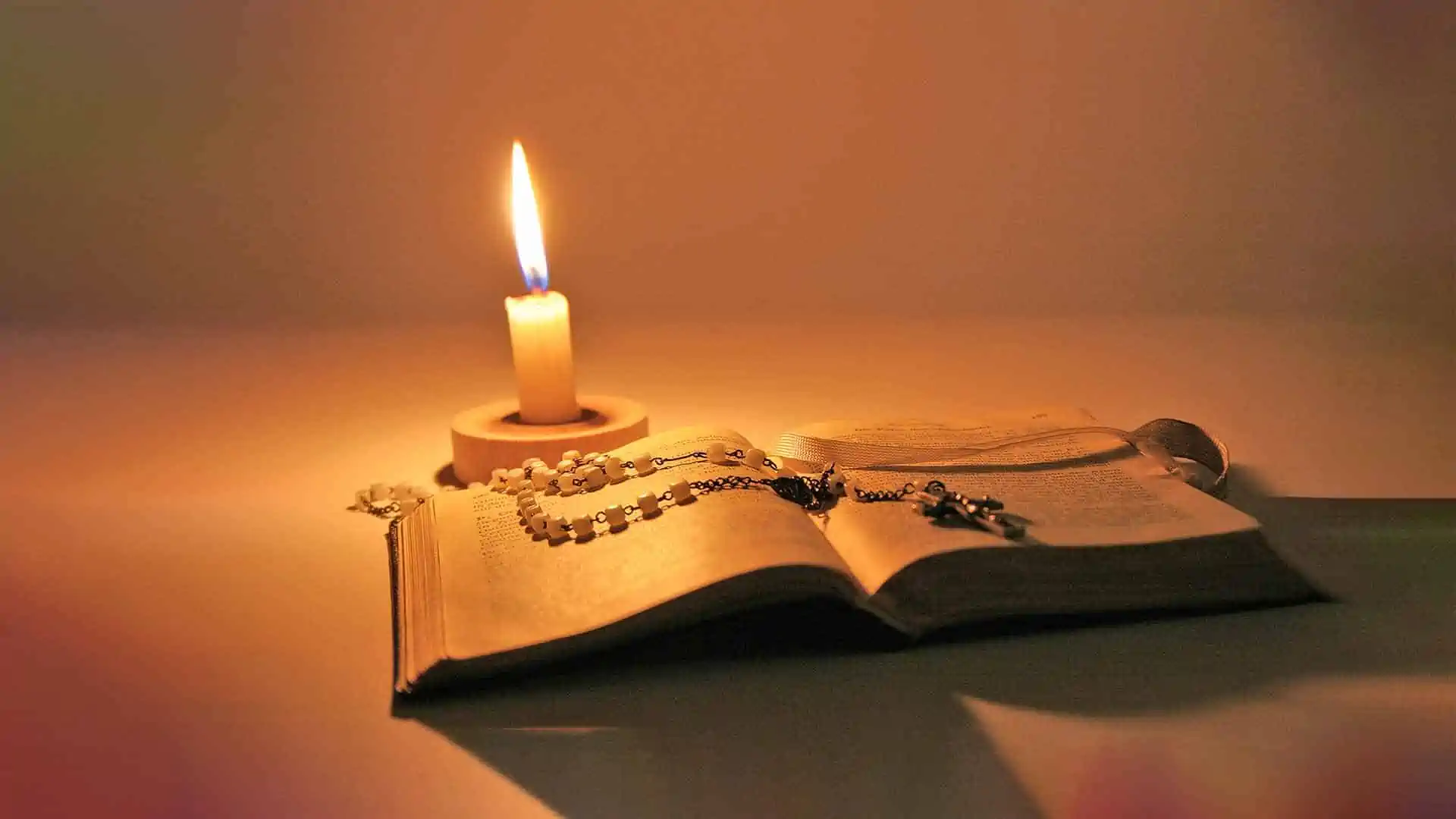 A Candle lit beside a Bible with a Rosary on the open pages.